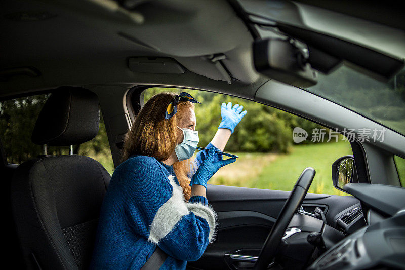 戴着防护面罩和手套开车的女人。世界大流行。保持安全。COVID - 19